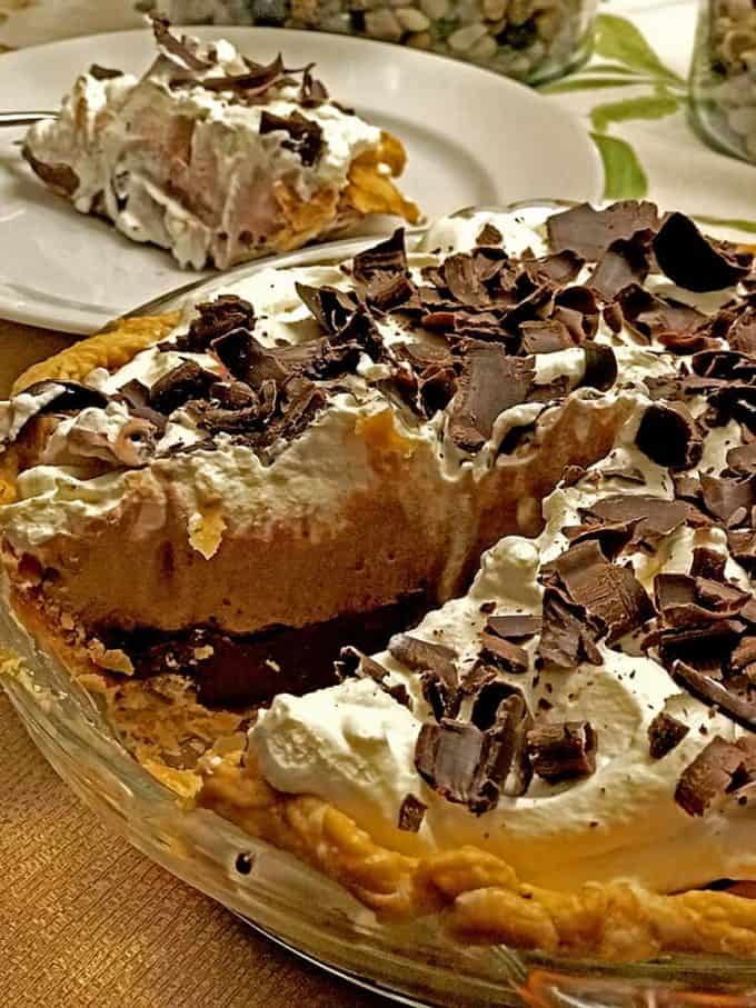 Baked pie with chocolate cream, plate slice behind on table