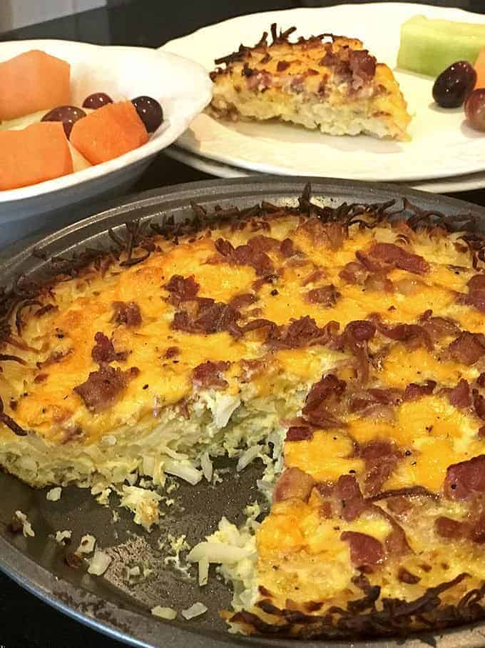 Cut fruit and slice of quiche on plate behind serving dish hash brown bacon quiche