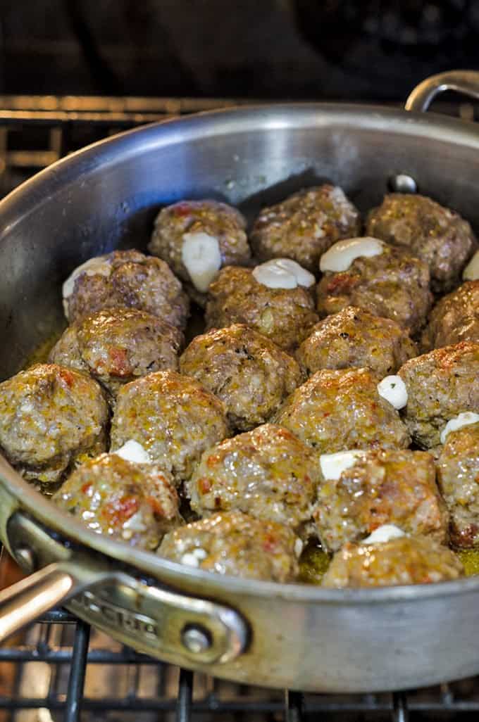 A packed skillet of meatballs being browned on stove