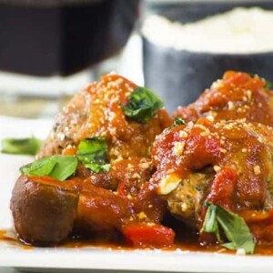 Close up side view of 3 sauced and garnished meatball on plate