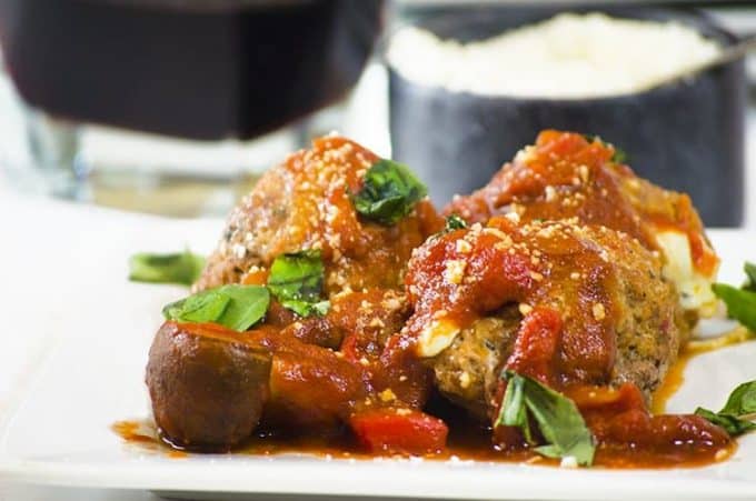 Close up side view of 3 sauced and garnished meatball on plate