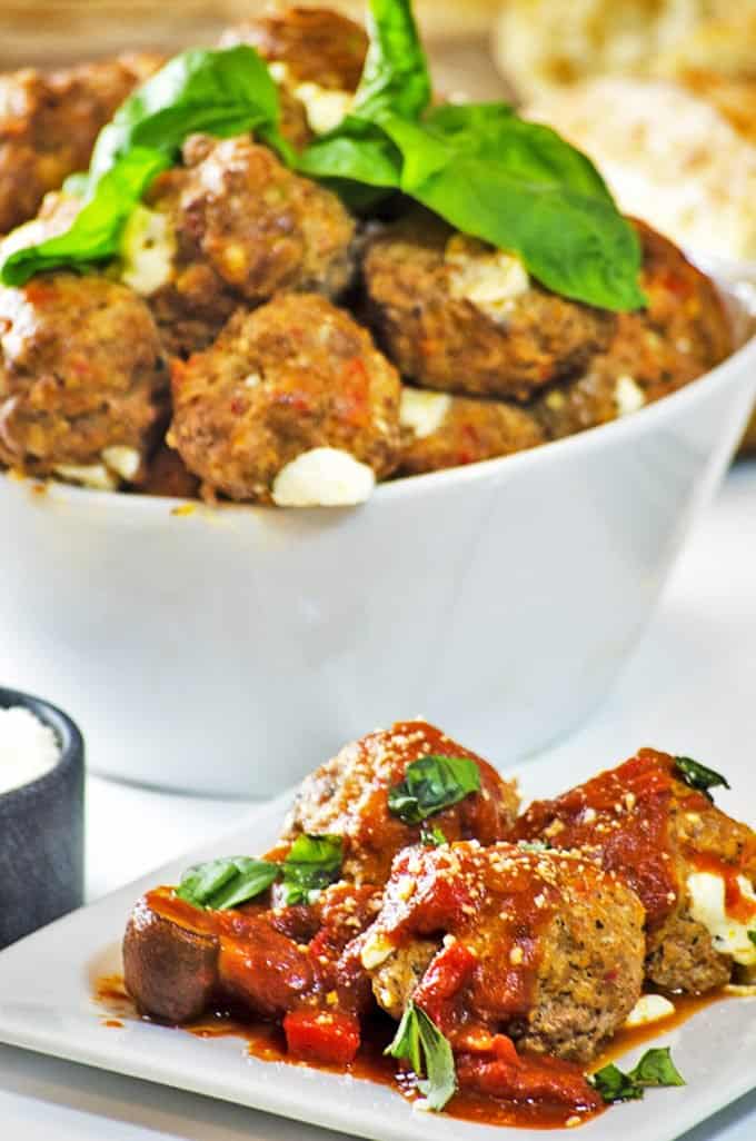 Fresh basil atop bowl of meatballs with some on plate, in front on table
