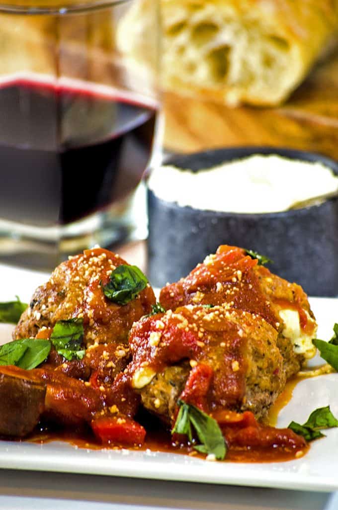 Close up 3 plated, sauced meatballs, grated cheese and red wine glass on table