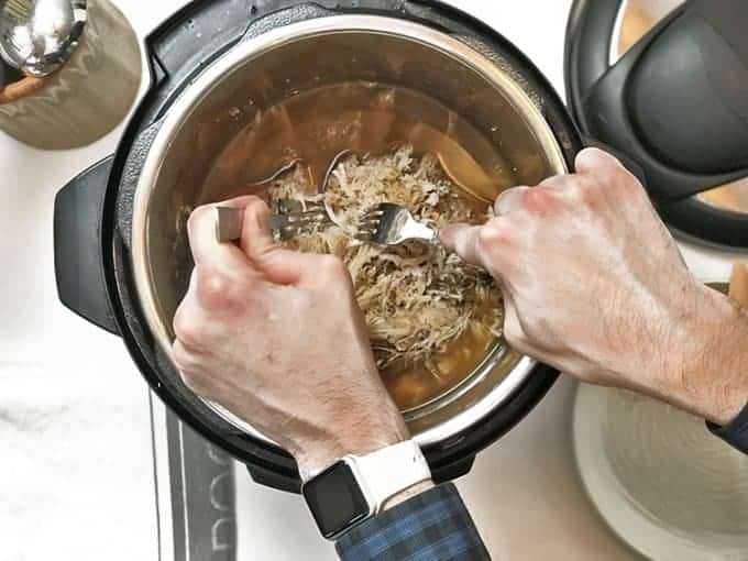 A person separating  meat in instant pot
