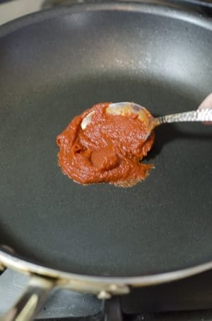 Someone putting spoon of tomato paste in center of non stick skillet