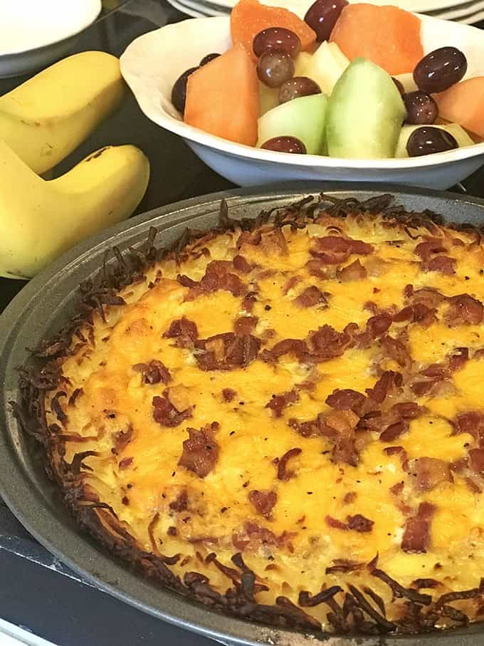 Whole potato quiche in front of bananas and bowl of cut fruit