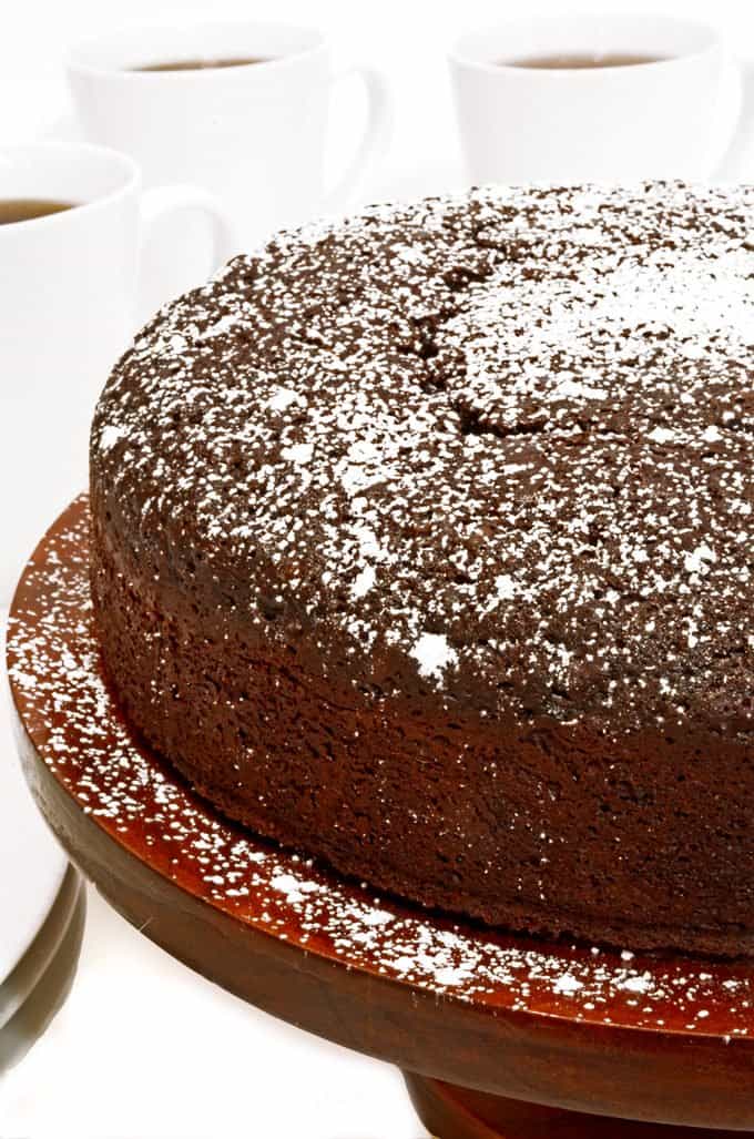 Chocolate cake dusted with powdered sugar, on a cake stand.