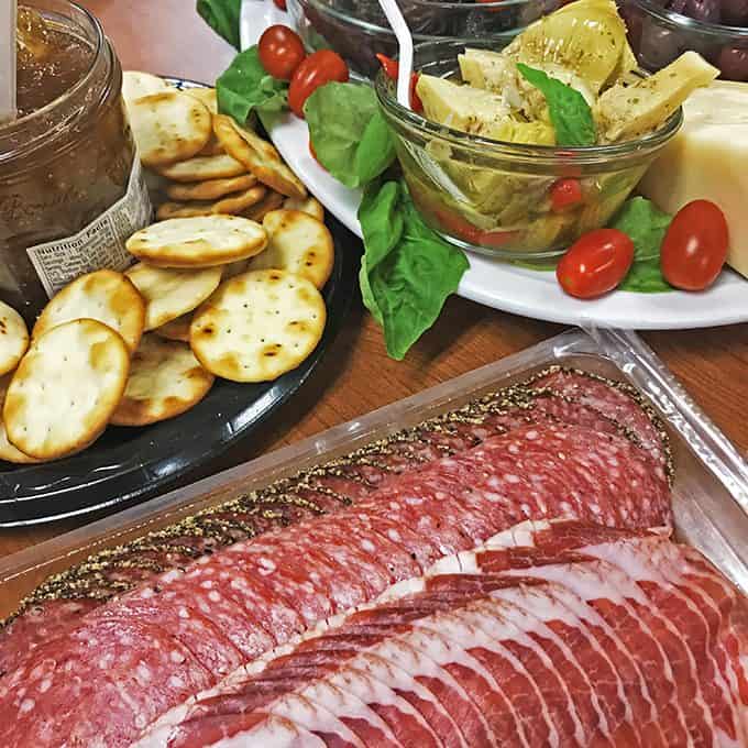 Assorted garnished foods for antipasto on table in serving trays and dishes