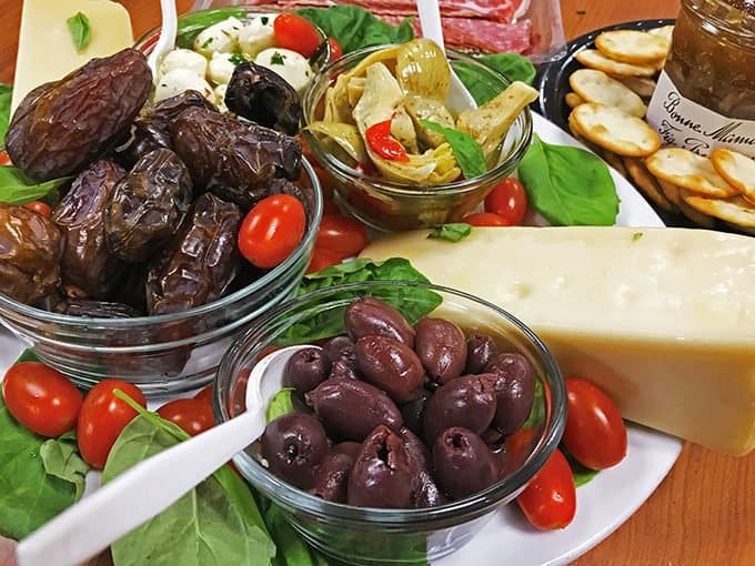 Foreground of dates, prunes and cheese wedge with crackers and artichoke in back