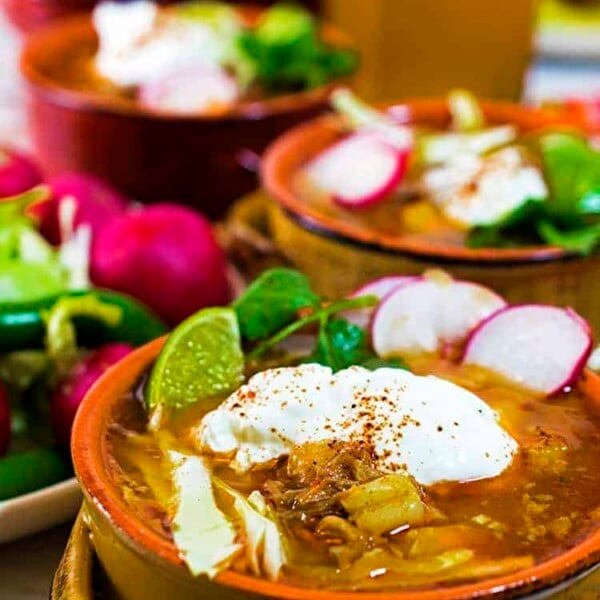 3 individual servings of posole garnished with cilantro, radish lime and sour cream