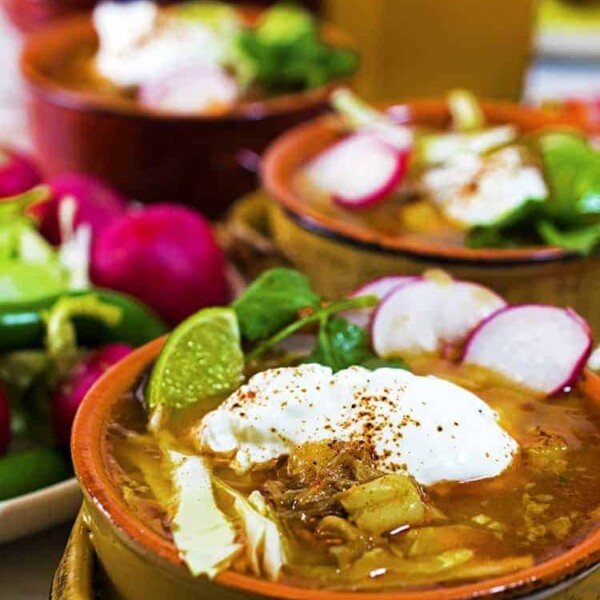 3 individual servings of posole garnished with cilantro, radish lime and sour cream