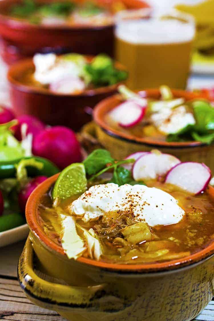 3 individual servings of posole garnished with cilantro, radish lime and sour cream 