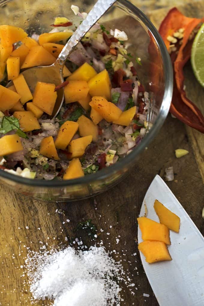 A bowl papaya being mixed with chopped vegetable on board with knife