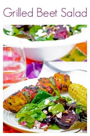 Bowl of salad in back of plated beet salad, corn and kabob on set table