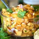 A close of papaya and Salsa in clear bowl with serving utensil