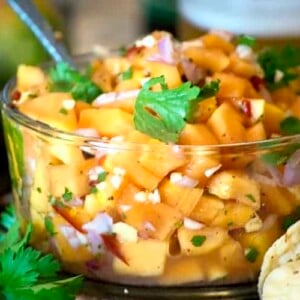 A close of papaya and Salsa in clear bowl with serving utensil