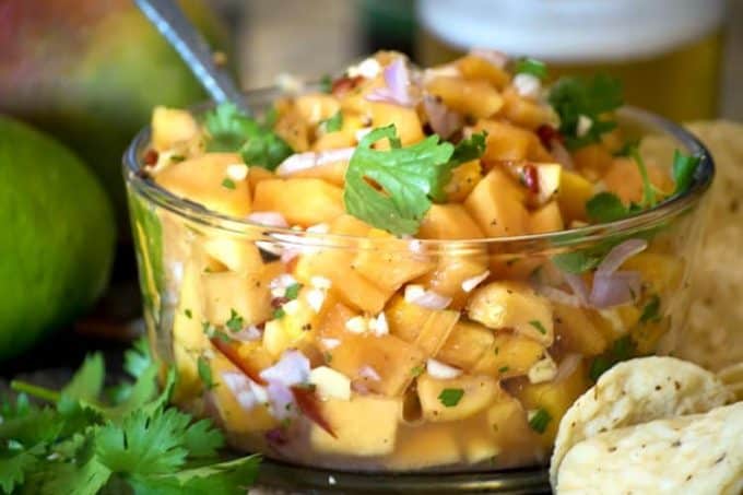 A close of papaya and Salsa in clear bowl with serving utensil