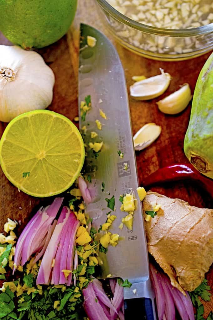 Knife, cutting board with ginger, garlic, red onion, lime and papaya