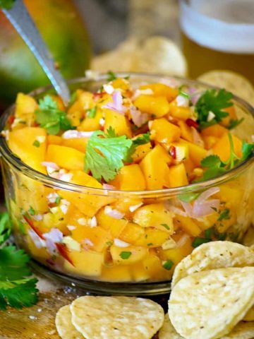 A glass bowl of papaya salsa serving spoon cilantro