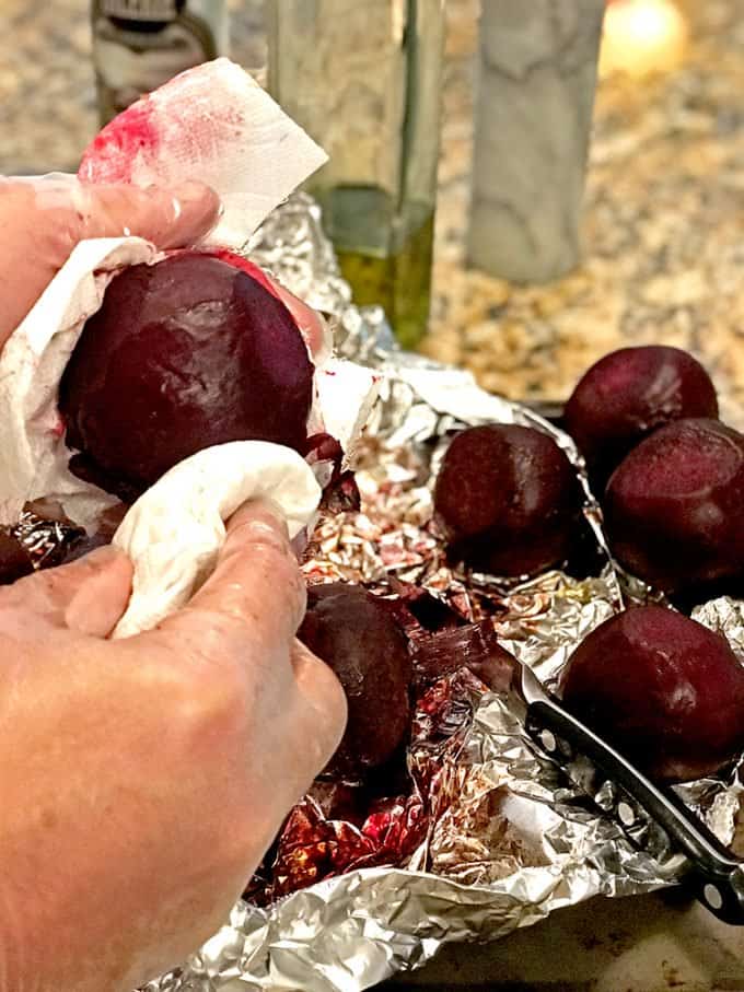 Someone rubbing skin off roasted beets with paper towel on aluminum foil