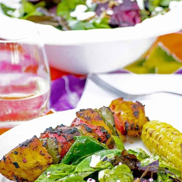 Plated kebab, corn cob, grilled beet salad, with salad bowl on tablecloth