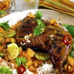 Jerked chicken quarter on plate of fruit and rice