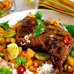 Jerked chicken quarter on plate of fruit and rice