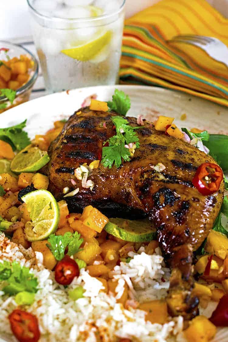 Jerked chicken quarter on plate of fruit and rice