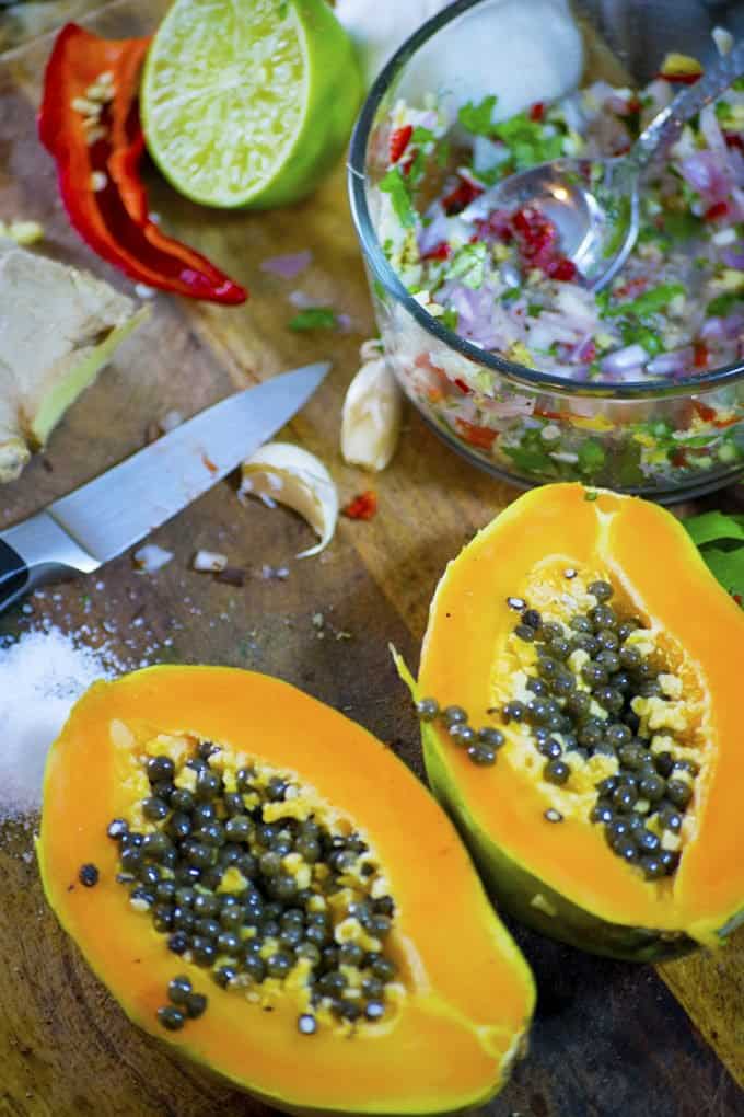 Bowl of chopped vegetables behind split papaya with knife on cutting board