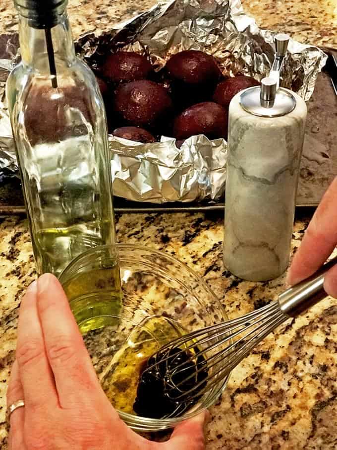 Someone whisking balsamic and olive oil with roasted whole beets in background