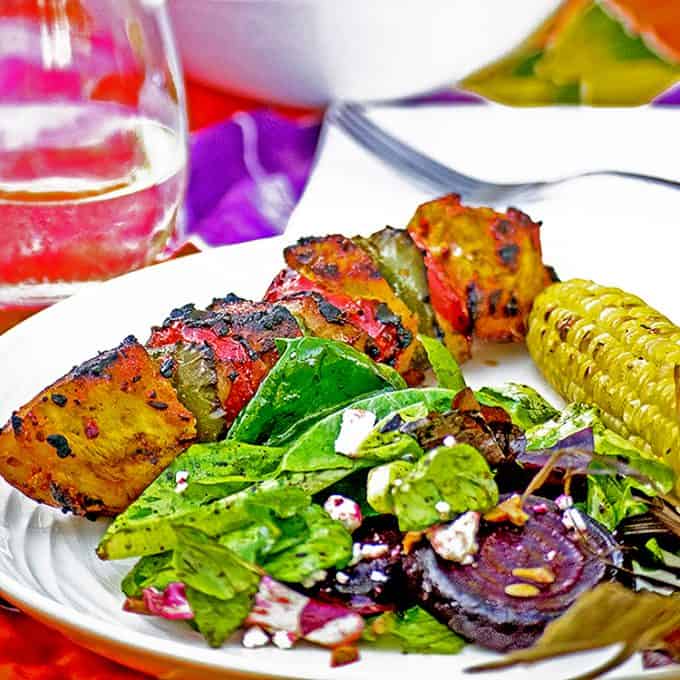 Dinner plate of roasted beet salad, corn, kabob on table with napkin and fork