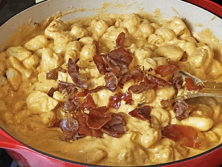 Skillet of pumpkin gnocchi in sauce with cooked proscuitto