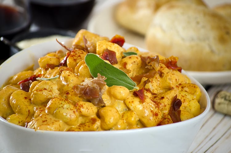 Close up Pumpkin gnocchi with herbs in serving bowl, bread in background 