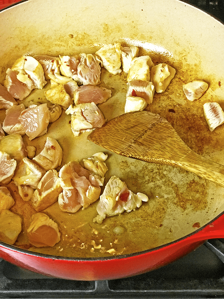 Raw diced chicken being sauteed in pan with wooden spoon