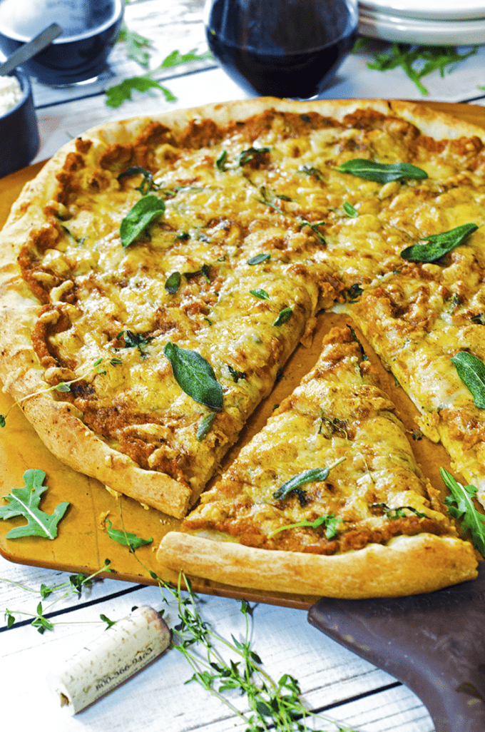 A cut pumpkin pizza with fresh herbs sitting on top of a wooden board