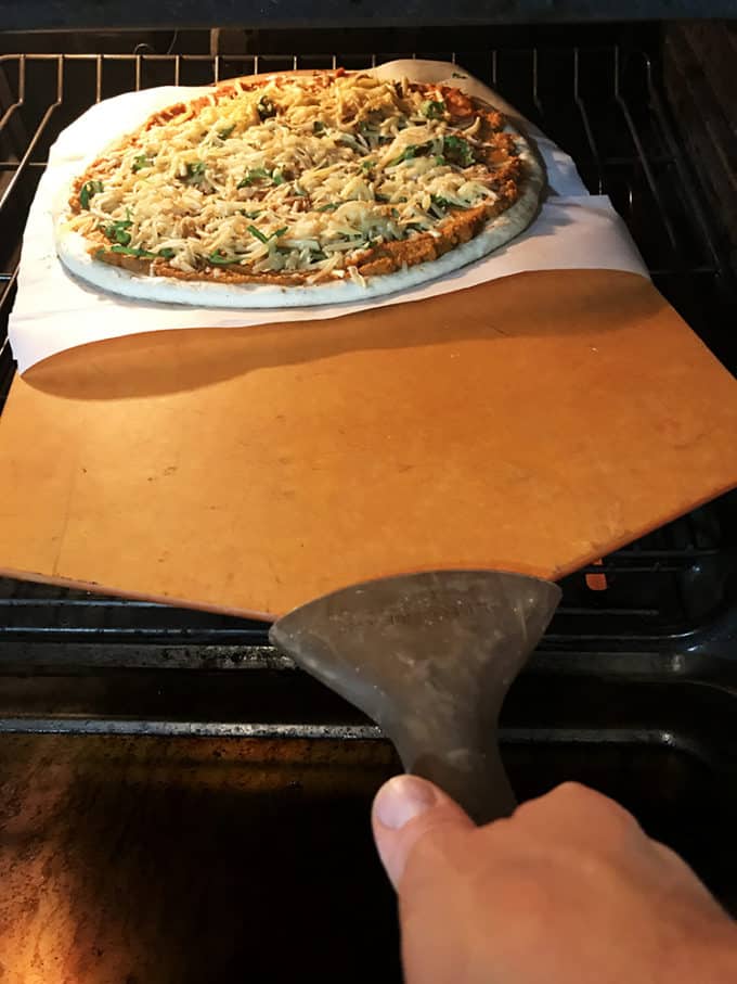 Pizza entering oven rack on parchment paper by way of peel