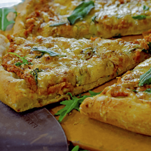 A slice of pumpkin pizza with fresh herbs atop board and peel