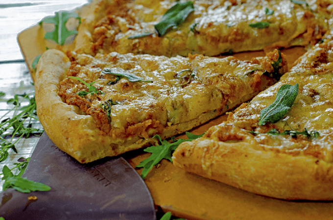 A slice of pumpkin pizza with fresh herbs atop board and peel