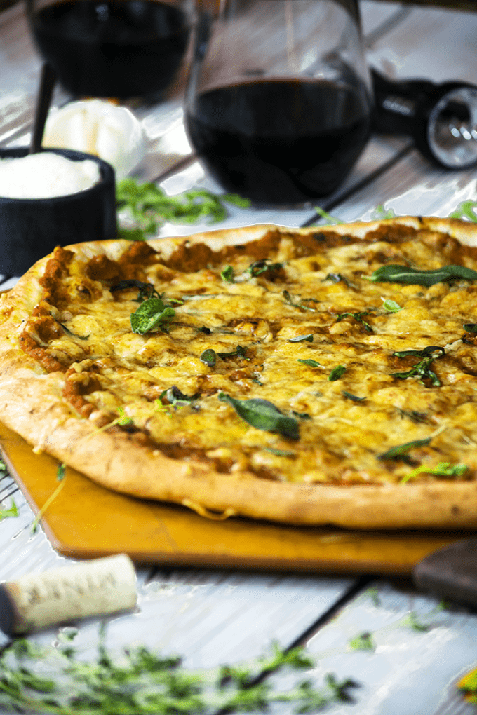 Side view of pumpkin pizza with fresh herbs on wood peel