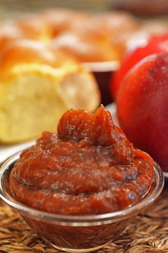 serving dish of apple butter with a dinner roll in the background.