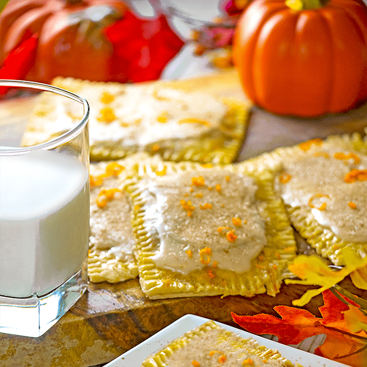 Glass of milk, pop tarts, pumpkins, fall leaves on parchment and wood