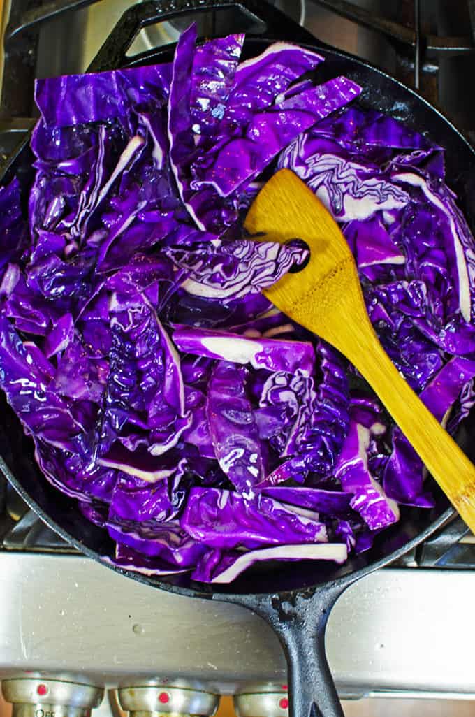 Stir fried cabbage in a skillet with a wooden spoon.