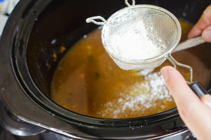 Adding flour to slow cooker gravy using a fine-mesh strainer.