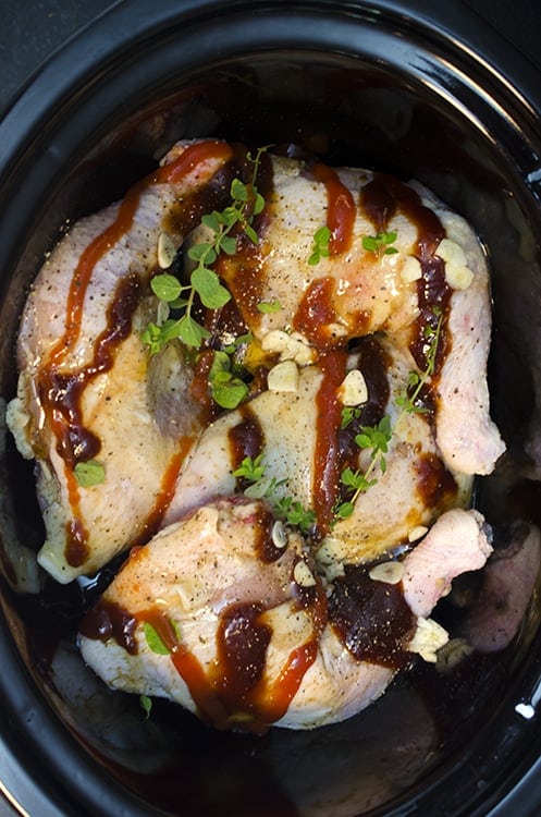Uncooked chicken thighs in a slow-cooker with barbecue sauce drizzeld over them.