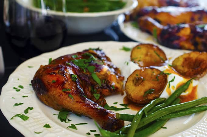 Plate of slow-cooker honey-garlic chicken thighs with potatoe slics and green beans.