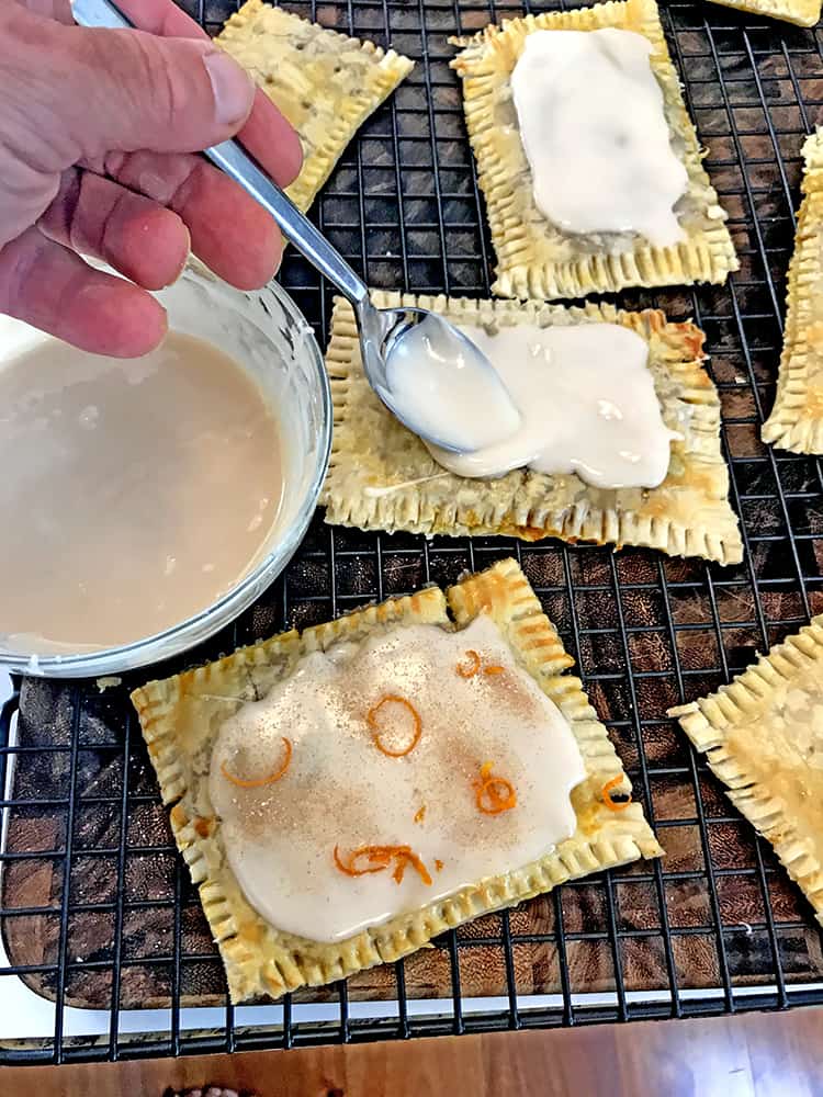 Someone icing pop tarts with spoon on cooling rack