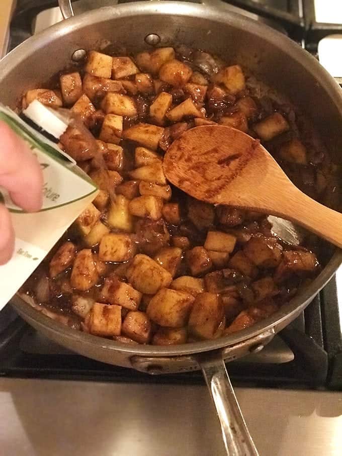 Someone adding liquid to cooking apples in pan on stove with wood spoon