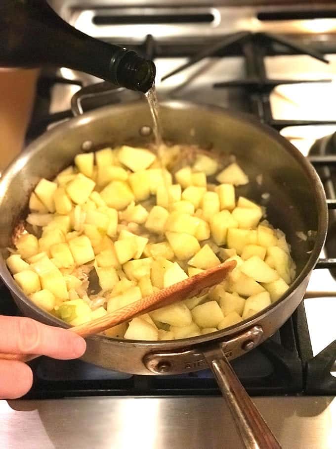 Liquid being added to cooking apples in a pan on stove with wooden spoon