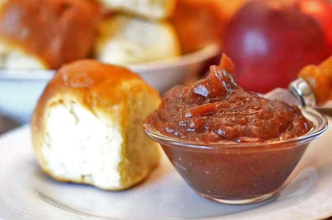 Dinner roll on a plate with dish of apple butter and butter knife.