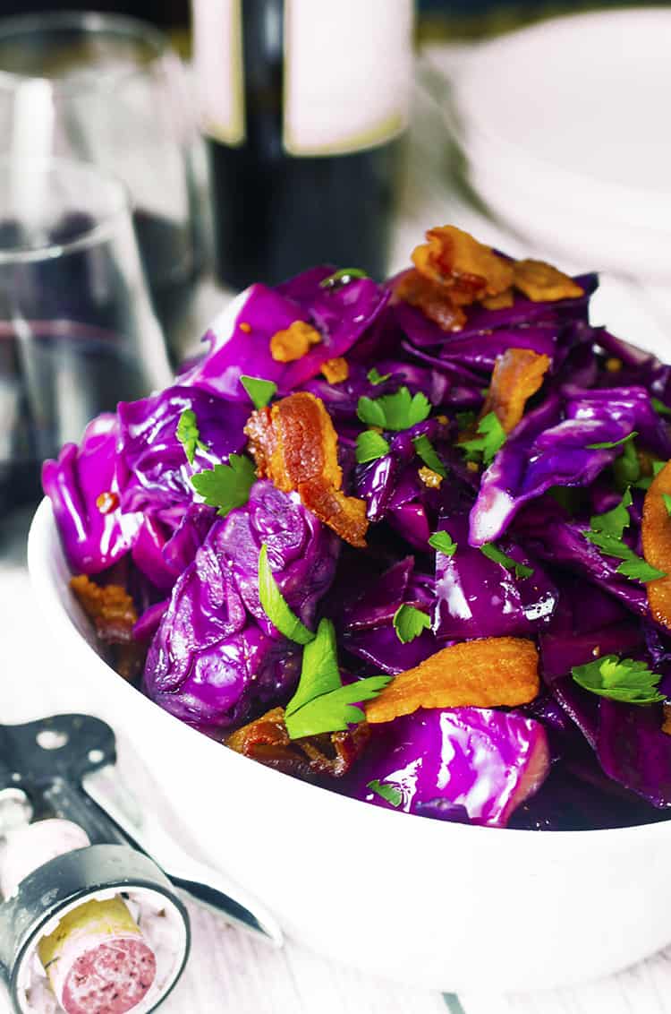 White bowl full of purple fried cabbage with pieces of bacon and Italian parsley.